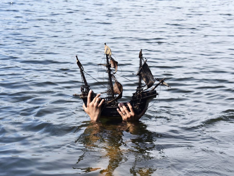 Hands hold a wooden toy ship out of the water.