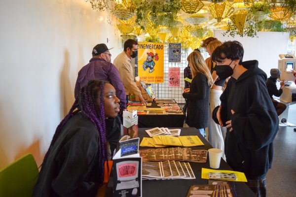 People standing and sitting at long tables filled with zines