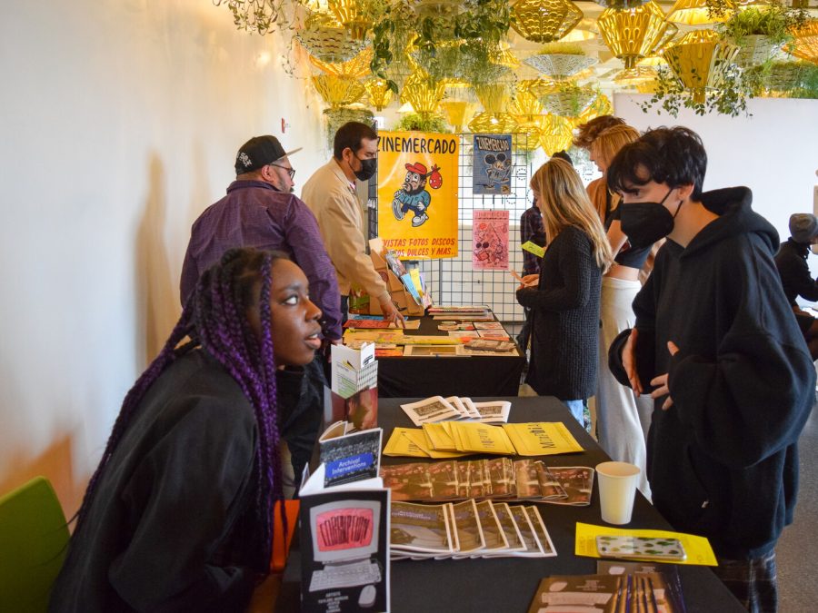 People standing and sitting at long tables filled with zines