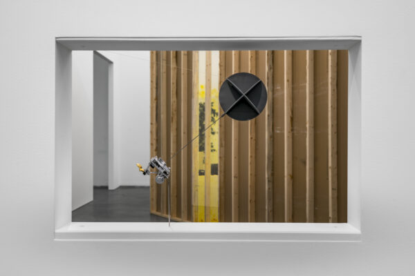 View through a cutout in a white wall to a room filled with artwork installations