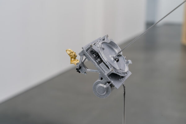 Closeup of a grey contraption holding a tiny golden statue of Saddam Hussein