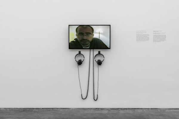 A video plays on a small screen connected to two sets of headphones hanging on a white wall