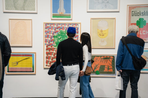 A small group of people look at artworks arranged gallery style on a white wall