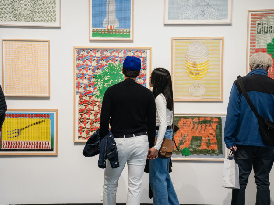 A small group of people look at artworks arranged gallery style on a white wall