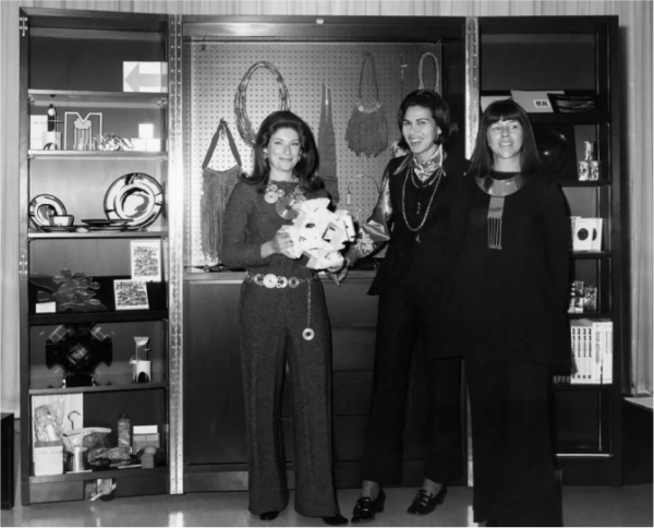 Black and white photo of three women in front of a small store featuring art and accessory objects