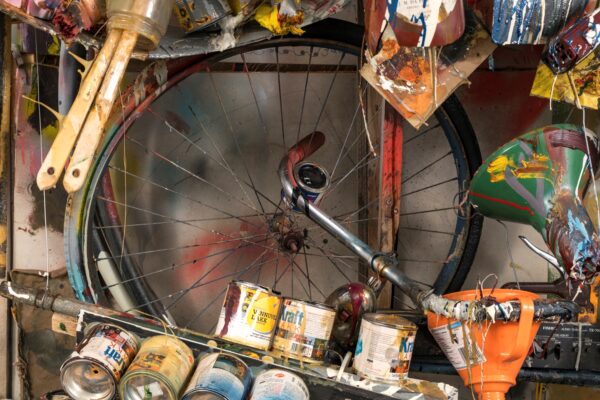 Parts of a bicycle are just decipherable amid a collage of old paint cans and other art making supplies