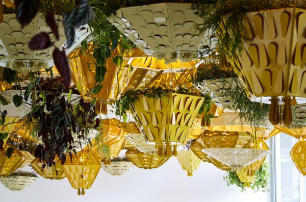 Yellow and white hanging planters featuring raindrop shaped cutouts and featuring tropical plants hang from a ceiling