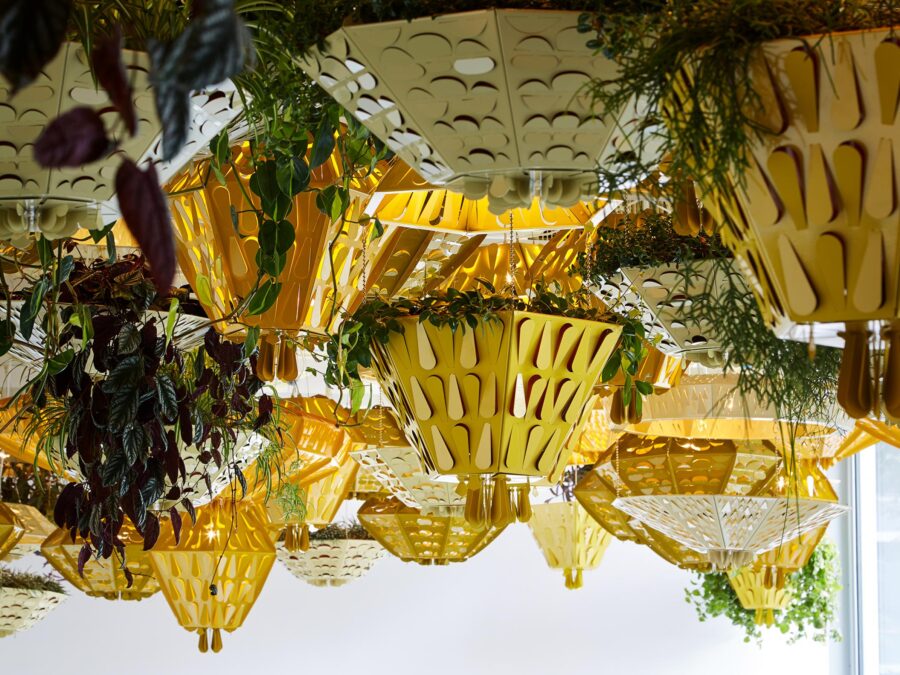 Yellow and white hanging planters featuring raindrop shaped cutouts and featuring tropical plants hang from a ceiling