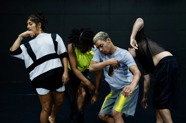 Four dancers in athletic wear pose in various positions, arms, knees, and bodies bent, against a black backdrop