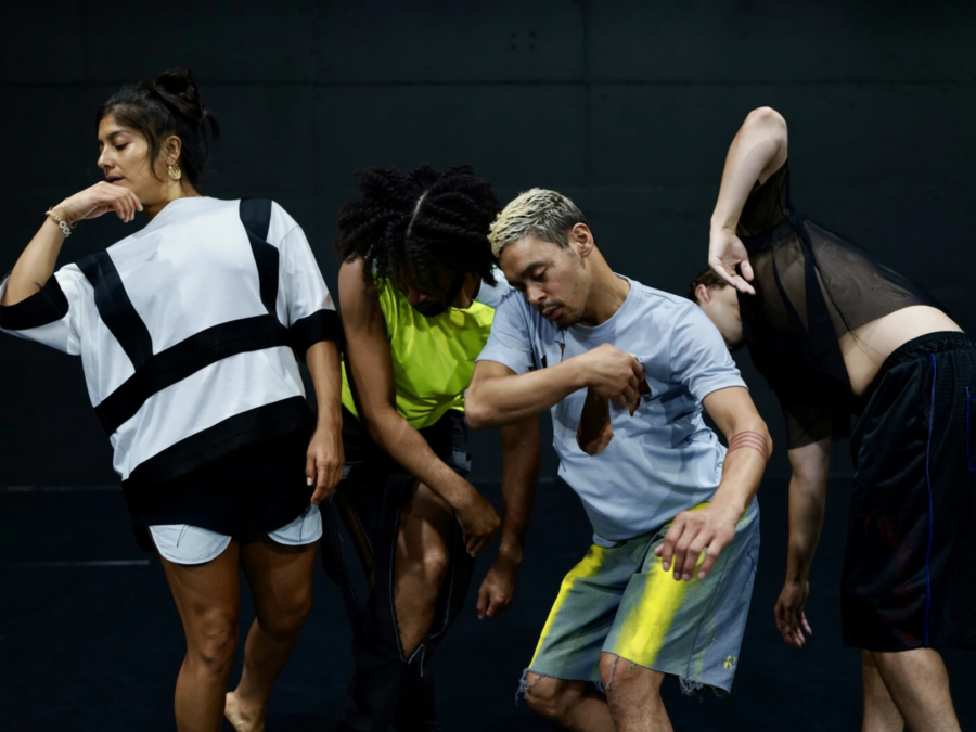 Four dancers in athletic wear pose in various positions, arms, knees, and bodies bent, against a black backdrop
