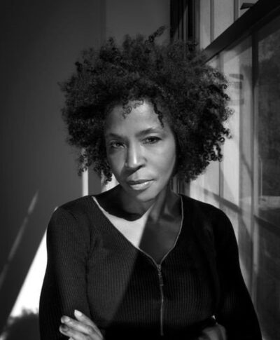 Black and white portrait of Lorna Simpson posing against a window that provides most of the lighting