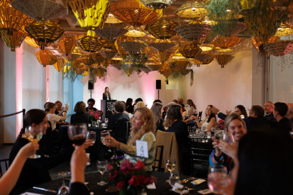 People cheer at several round tables in a plant-filled room