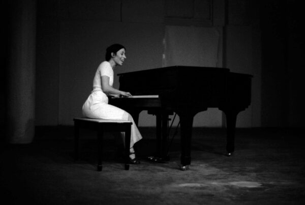A black and white photo of a person in a white dress playing at a grand piano