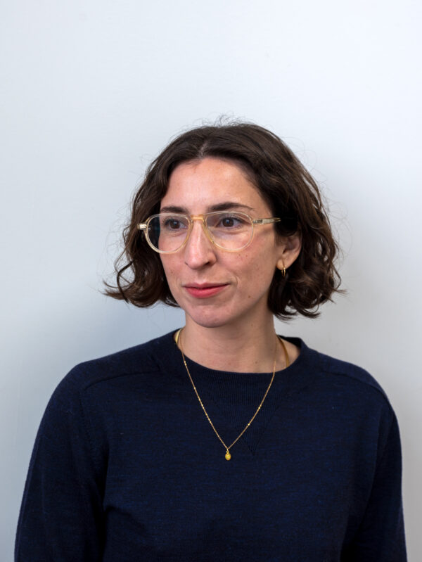 Portrait of a female-presenting person with brown hair cut in a bob style wearing glasses, a black shirt, and a necklace