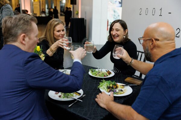 A group of four people toast at a table during a salad course