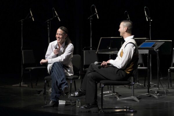 Two people sit on a stage holding microphones