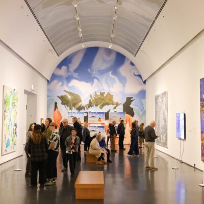 People standing in a large, vaulted gallery with artwork on all walls