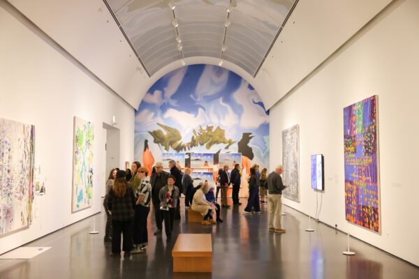 People standing in a large, vaulted gallery with artwork on all walls