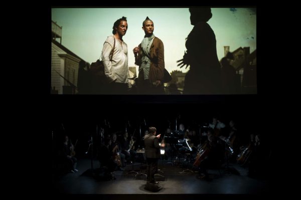 A film is screened above a live band.