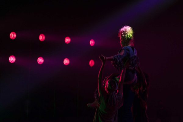 Eight rose-colored spotlights illuminate a person on a darkened stage