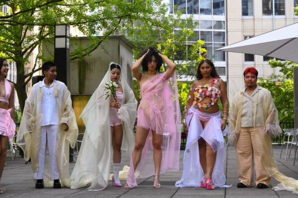 A group of six models displaying a variety of unique, colorful outfits in an outdoor fashion show.