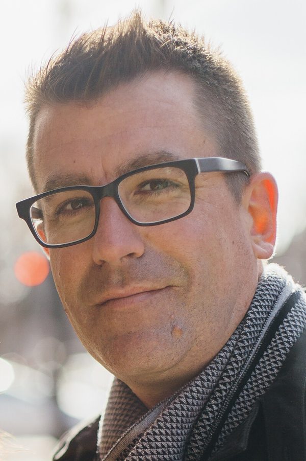 Portrait of a light-skinned man wearing glasses and a grey scarf.