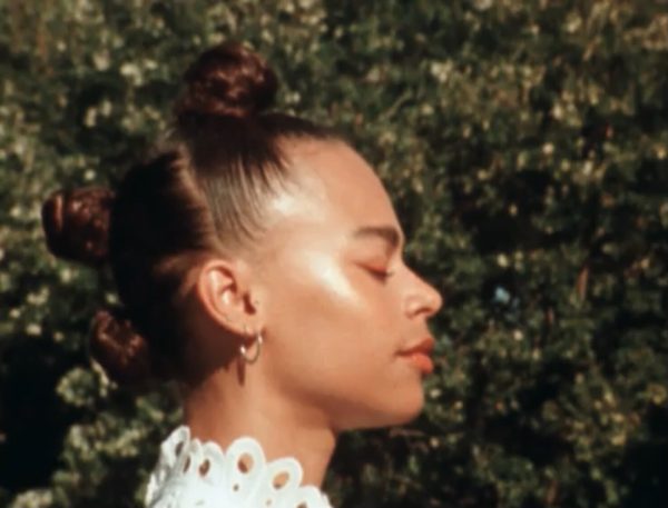 Profile of a person with their hair done up in three buns outside with their eyes closed