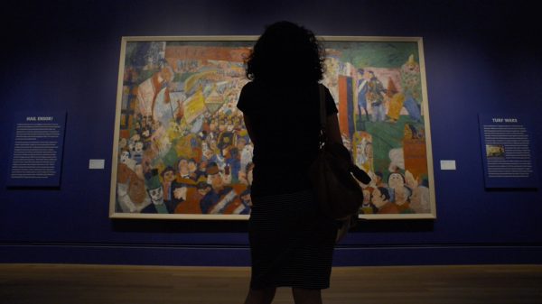 The outline of a person standing in front of a large painting on an indigo wall