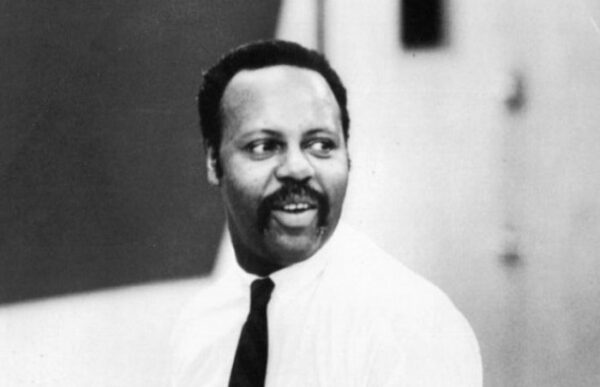Black and white archival photo of a brown-skinned man wearing a white shirt and tie