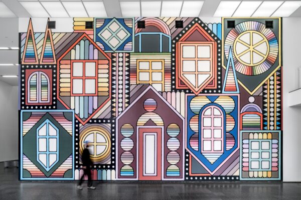 A two-story wall filled with a illustrated mural of colorful dormers, some upright, some upside down, featuring different style windows around a door in the middle.