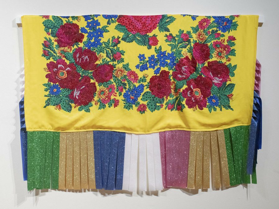 A yellow shawl covered in red and blue flowers with green, tan, blue, white, and pink fringe