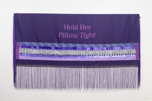 A purple shawl with ribbon and fringe embroidered with the words Hold Her Pillow Tight