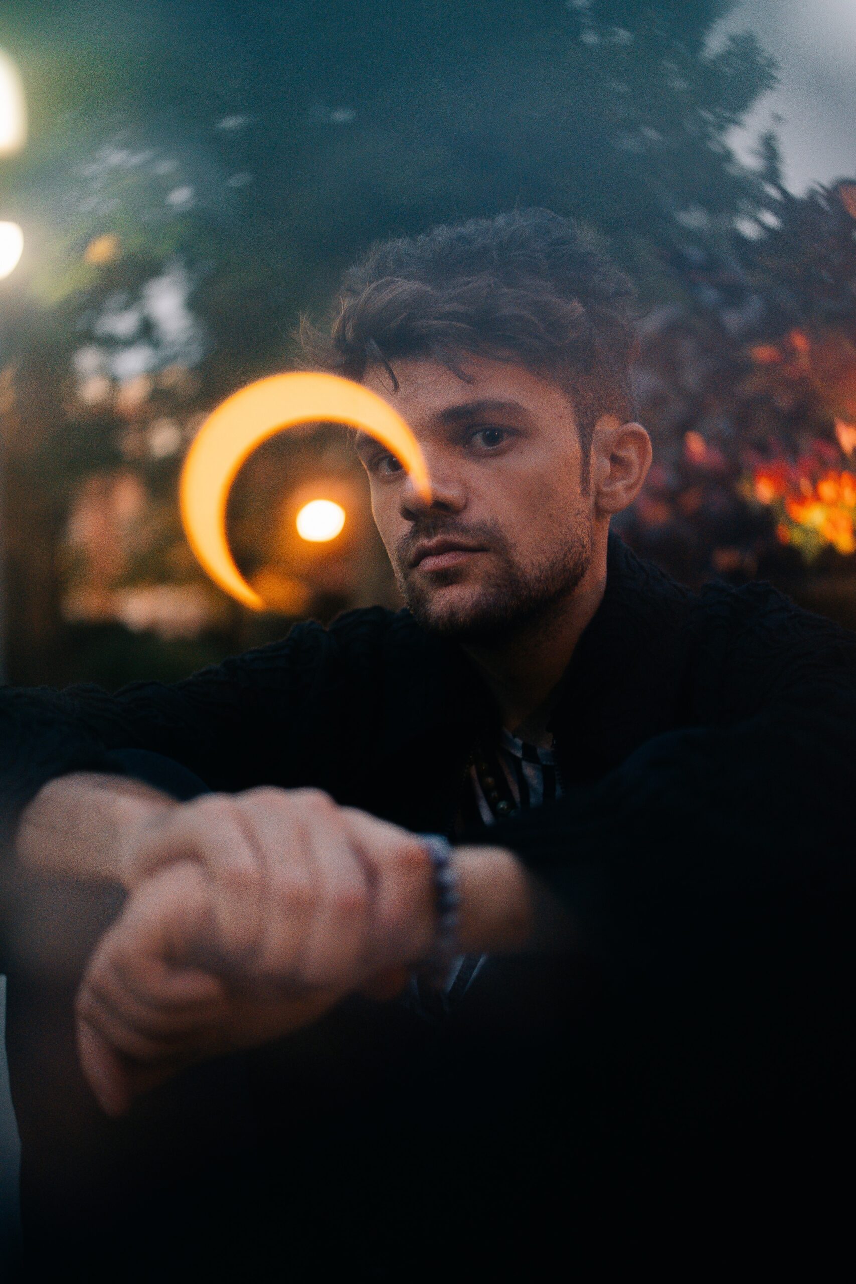 Portrait of a light-skinned male presenting person outdoors. A light reflection obscures part of their face