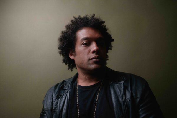 Moody portrait of a male-presenting person wearing all black against a grey backdrop