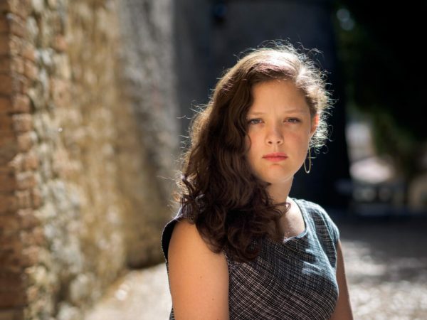 Portrait of a woman near a brick wall with the sun shimmering off her dark brown hair.