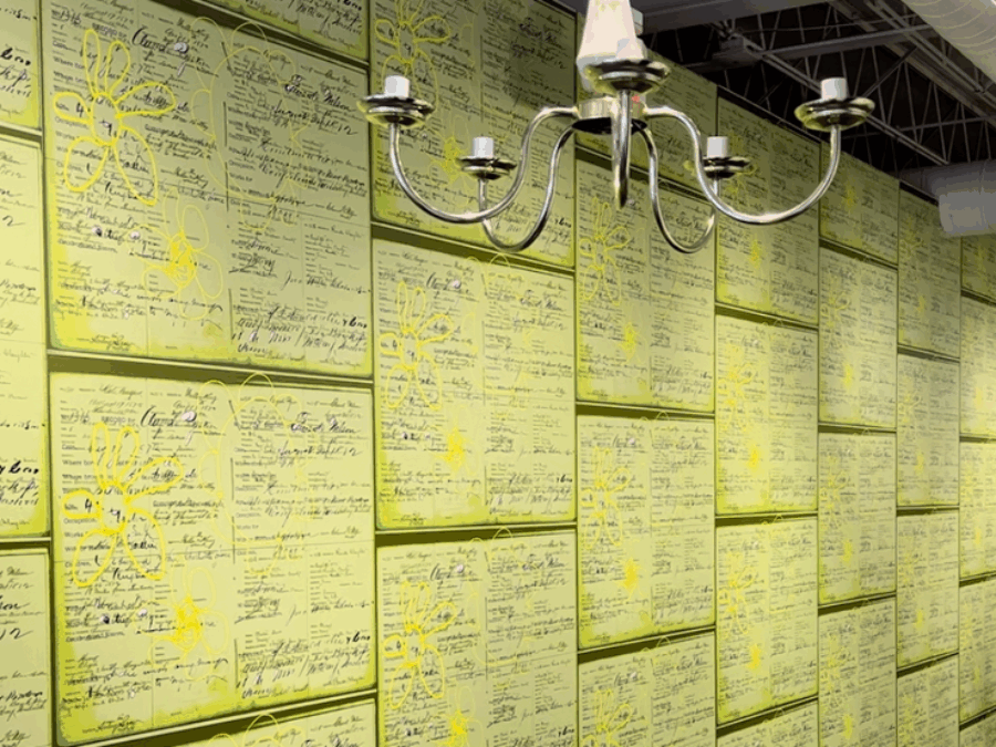 Enlarged facsimiles of old forms covered in daisies cover a wall of a room with an unused chandelier hanging from the ceiling