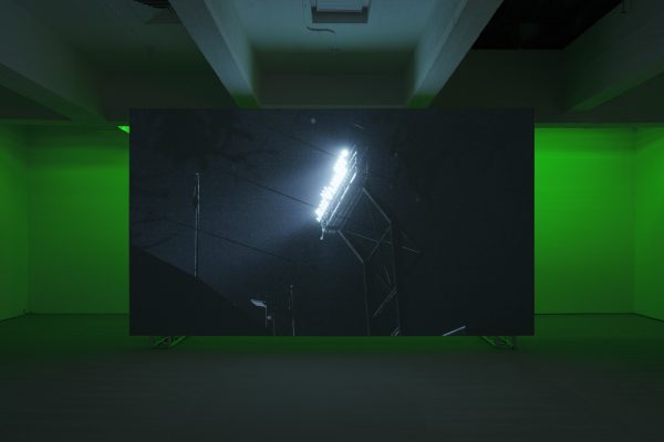 in the middle of a darkened room a screen displays a closeup of stadium lights with black lines running diagonally through the whole image. The wall behind the screen glows green from recessed lights.