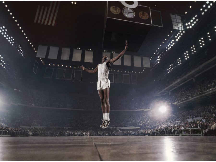 a basketball player hovering above our line of sight in a cruciform position in an arena filled with spectators