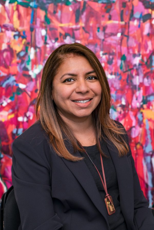 Portrait of a woman wearing a gray blazer and shirt against a colorful background.