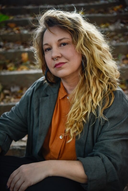 Portrait of a woman with thick, blond hair sitting on a set of concrete steps