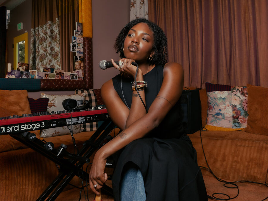 Portrait of a brown-skinned female-presenting person holding a microphone next to an electronic keyboard