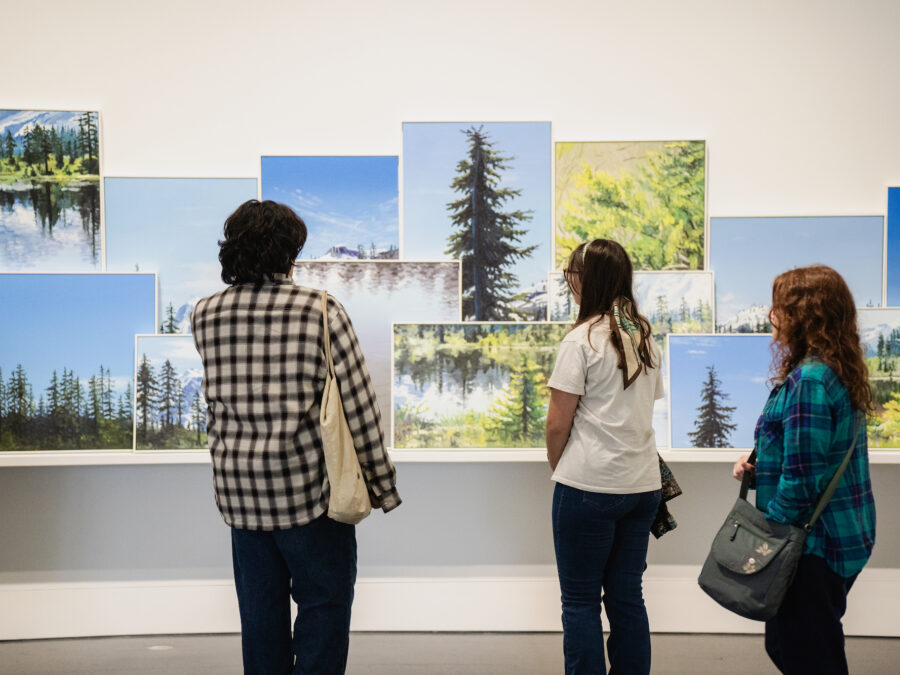 Three people look at various sized paintings layered to look like a landscape.