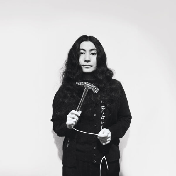 Black and white archival photo of Yoko Ono holding a hammer attached to a string