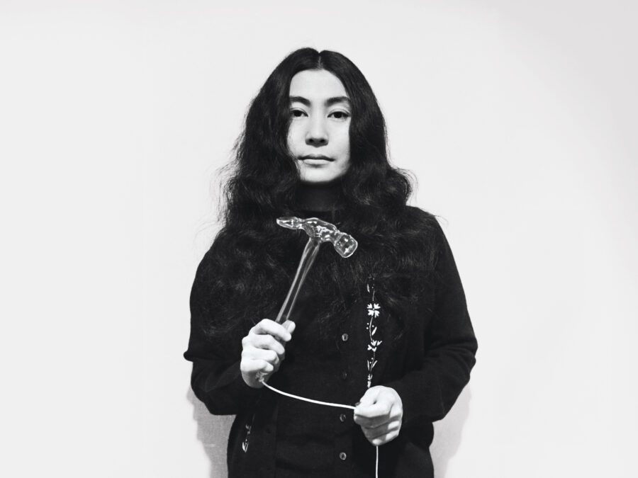 Black and white archival photo of Yoko Ono holding a hammer attached to a string