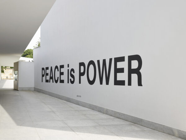 View down a long outdoor hallway with large black text on a white wall reading Peace is Power