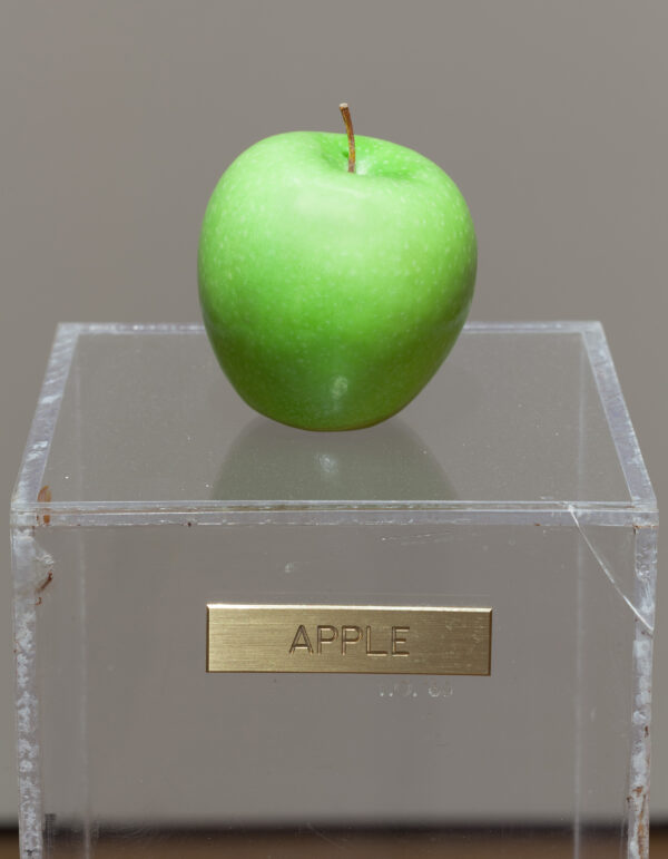A green apple on a plexiglas pedestal with a gold plaque reading Apple