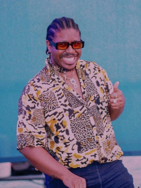 A male-presenting person in sunglasses and a fun printed short-sleeved shirt giving a thumbs up