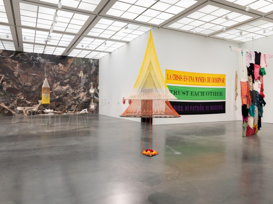 A large, white-walled gallery space with several large, colorful works of art, many made out of fabric, installed throughout the room.