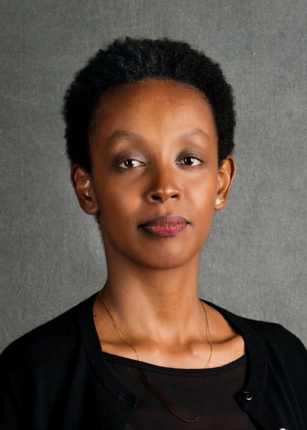 Portrait of a female-presenting person with light brown skin and short black hair against a grey backdrop