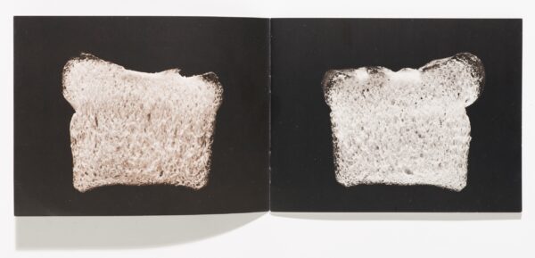 An open book featuring a slice of bread against a black background on each page.